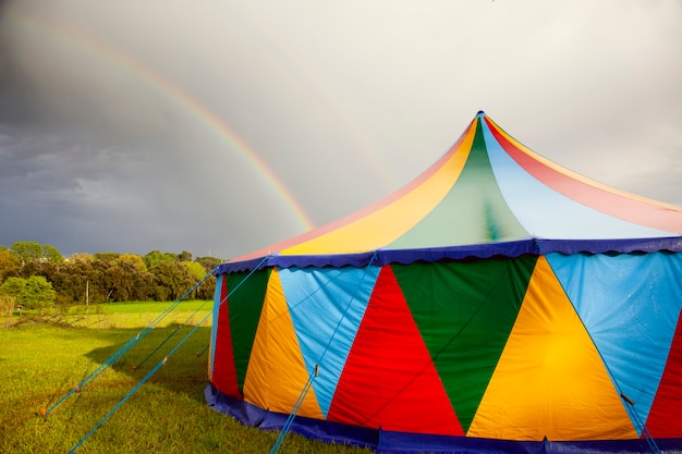 Tenda de circo colorida em dia chuvoso com arco-íris no céu