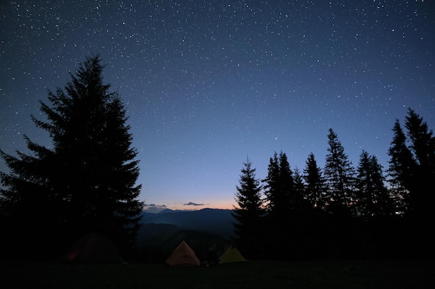 Tendas de acampamento brilhantemente iluminadas brilhando no acampamento em montanhas escuras sob estrelas noturnas cobertas de céu Estilo de vida ativo e conceito de viagem