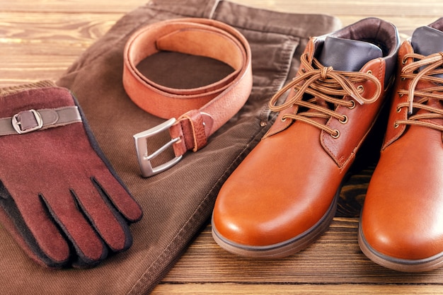 Tendência da moda para jeans, sapatos de couro, cinto de couro, luvas na superfície de madeira.