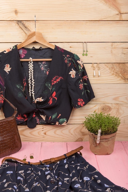 Tendências da moda Blusa crop top preta com estampa floral pendurada no cabide saia azul bolsa de cinto