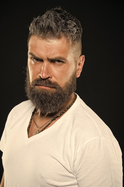 Tendencias de diseño de cabello Hipster serio con barba larga y cabello elegante sobre fondo negro Hombre barbudo con vello facial sin afeitar Chico brutal con barba en forma y cabello con bigote