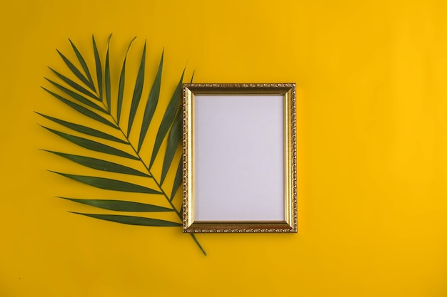 Tendido plano con marco de fotos vacío y rama de palmera sobre fondo amarillo