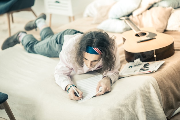 Tendo período produtivo. Artista de cabelos escuros deitado na cama trabalhando na criação enquanto está sozinho em casa