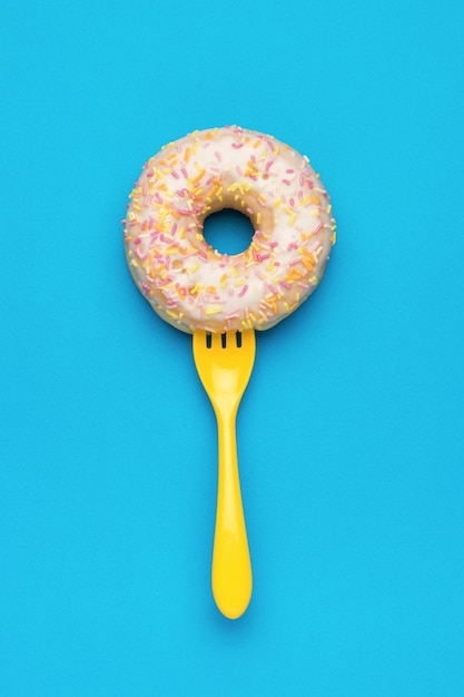 Un tenedor amarillo en un donut glaseado sobre un fondo azul El concepto mínimo de horneado popular