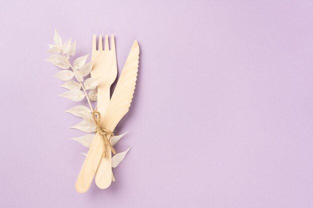 Tenedor de cubiertos de madera y cuchillo para llevar con una rama seca de una flor sobre fondo lavanda