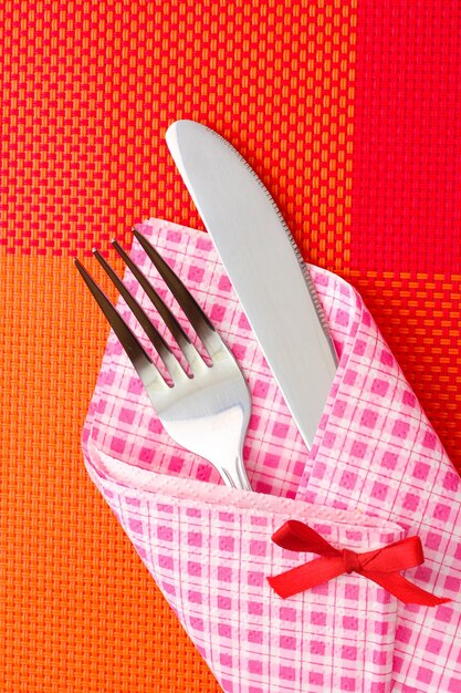 Foto tenedor y cuchillo en un paño a cuadros con un lazo sobre un mantel rojo