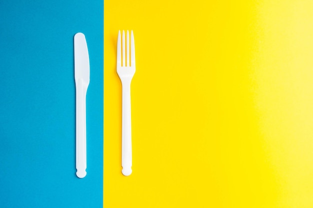 Tenedor y cuchillo de plástico blanco sobre fondo amarillo y azul