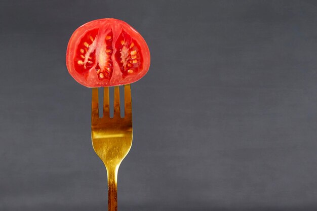 En un tenedor dorado, un tomate rojo sobre un fondo gris Comida creativa o verduras Concepto de comida saludable