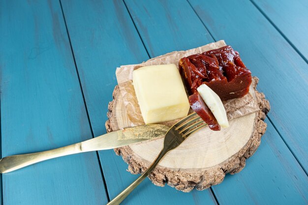 Tenedor dorado con trozos de dulce de guayaba y queso en un plato de madera junto a una vista de cuchillo