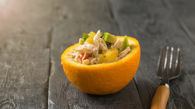 Un tenedor con mango de madera y media naranja con ensalada en una mesa de madera