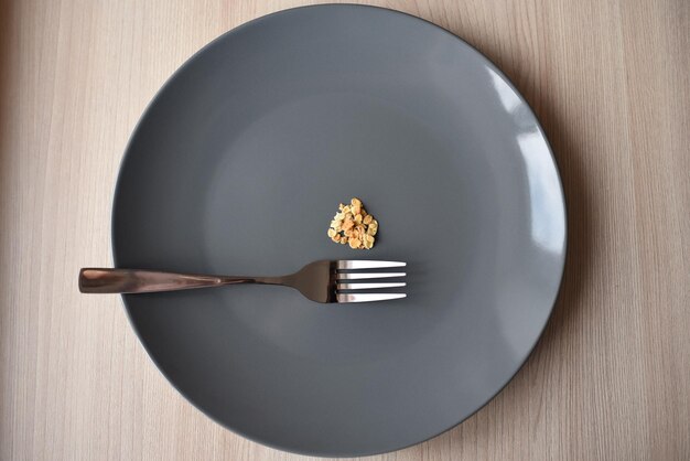 Foto un tenedor de metal y un plato gris con una pequeña porción de comida