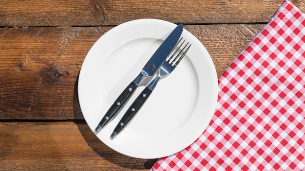 Foto tenedor y navaja en un plato blanco y servilleta sobre la mesa de madera