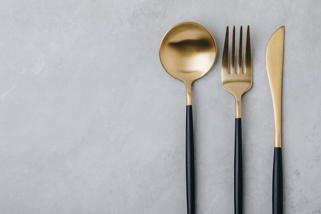 Foto tenedor de oro, cuchillo y cuchara en la vista superior de fondo de piedra gris