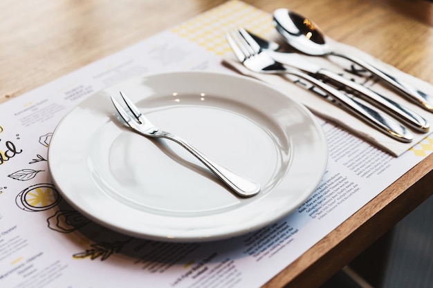 Tenedor de ostra con cubiertos: Cuchara, tenedor y cuchillo en un plato de cerámica blanca. Artículos de comida bañados en plata.