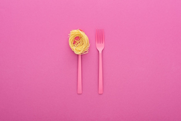Foto tenedor de plástico rosa y pasta en cuchara rosa sobre fondo rosa
