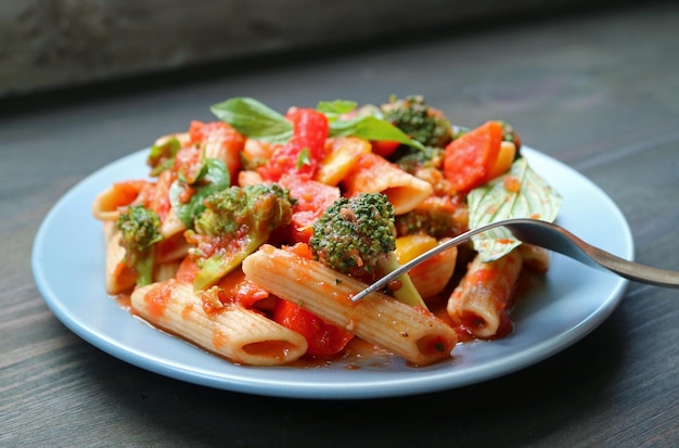 Tenedor recogiendo Penne sabroso con verduras asadas en salsa de tomate y albahaca