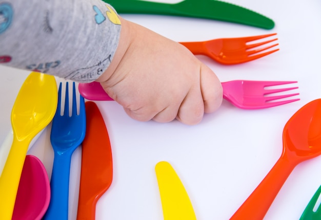 Tenedor rojo en la mano del niño y vajilla de colores alrededor.