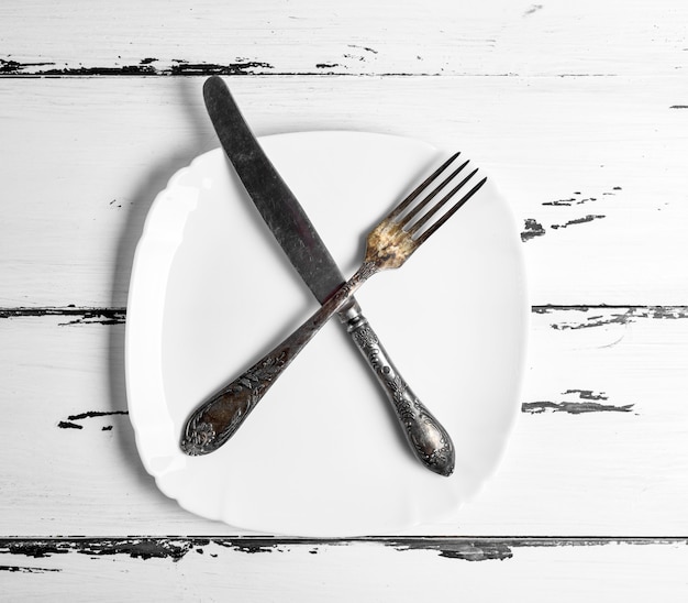 Foto tenedor vintage de hierro con un cuchillo sobre una placa cuadrada blanca en blanco