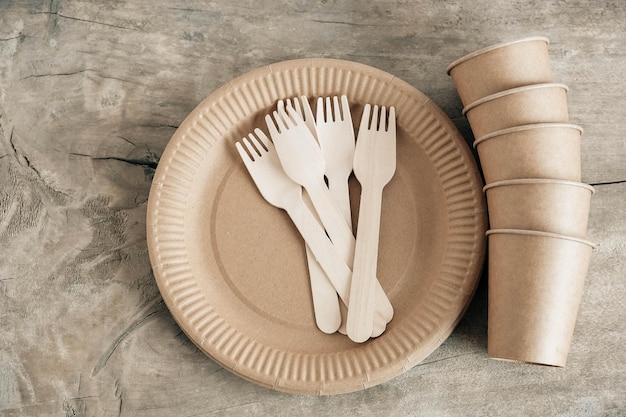 Tenedores de madera y vasos de papel con platos sobre fondo de madera. Vajilla desechable ecológica. También se utiliza en comida rápida, restaurantes, comida para llevar, picnics. Vista superior. Copiar, espacio vacío para texto