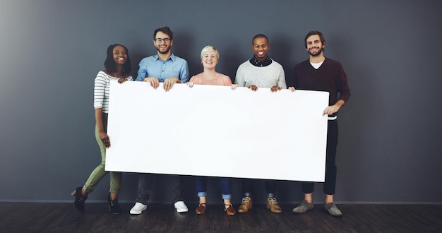 Tenemos algo para ti Foto de estudio de un grupo diverso de personas sosteniendo un cartel en blanco sobre un fondo gris