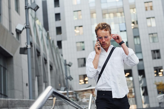 Tener una conversación por teléfono Un joven elegante vestido con buena ropa está al aire libre en la ciudad durante el día