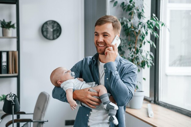 Tener una conversación por teléfono Padre con niño pequeño está adentro en la oficina