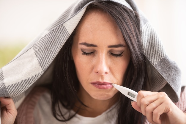 Tener frío a la mujer mide la fiebre sosteniendo el termómetro en la boca.