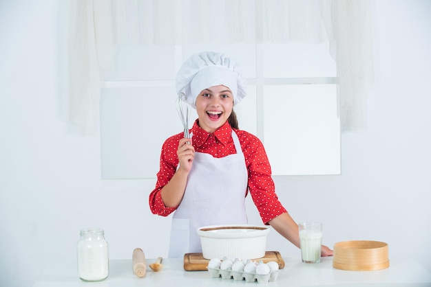 Tener una idea de tiempo para comer niño feliz cocinando en la cocina hornear galletas en la cocina niño panadero profesional y experto en uniforme de chef y sombrero niña adolescente preparando masa haciendo pastel por receta