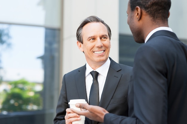 Foto tener una pausa para el café para conversar. dos hombres de negocios alegres hablando y gesticulando mientras está de pie al aire libre