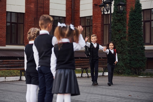 Tener una reunión. Grupo de niños en uniforme escolar que está al aire libre junto al edificio de educación.