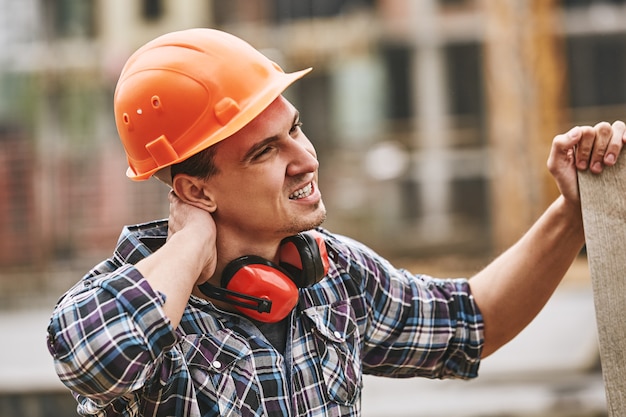 Tenga cuidado, trabajador de la construcción en casco protector que siente dolor de cuello mientras trabaja en la construcción