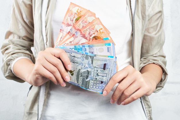 Tenge. Una chica con una camiseta blanca sosteniendo un montón de billetes kazajos de cerca.