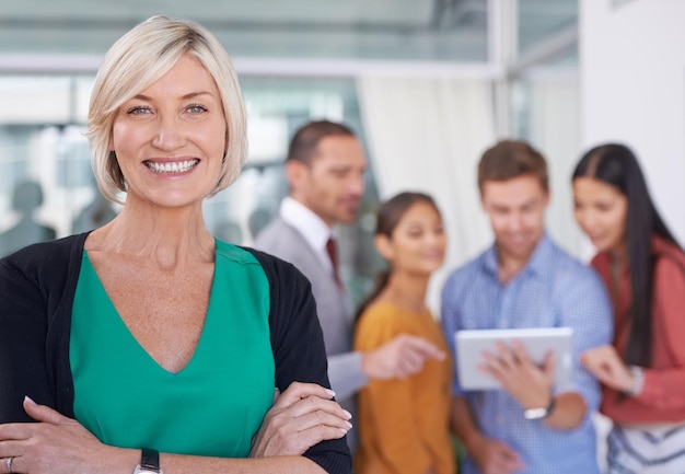 Tengo grandes esperanzas puestas en este equipo Un retrato de una mujer de negocios feliz parada en una oficina con sus compañeros de trabajo al fondo