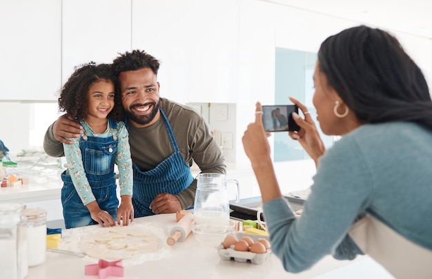 Tengo que capturar este momento. Captura recortada de una joven irreconocible tomando una foto de su esposo y su hija horneando en la cocina de su casa.