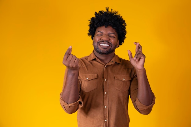 Tengo que ganar Alegre joven moreno aprieta los dientes levanta los dedos cruzados pide un deseo deseable pelo rizado mestizo afro brasileño espera buenas noticias sobre la pared amarilla