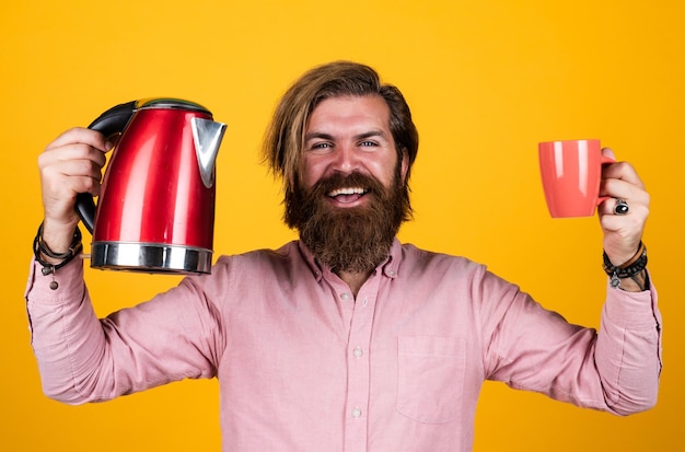 Tenha um dia feliz, beba chá quente homem barbudo assistente de loja apresentando utensílio de cozinha útil nas tarefas domésticas macho carismático maduro usa chaleira elétrica cara com barba e bigode fazer chá