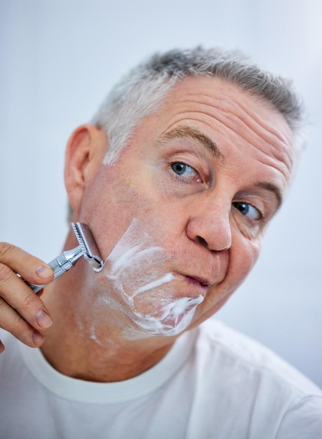 Tenho que me concentrar ao fazer a barba Foto de um homem maduro fazendo a barba no banheiro de casa