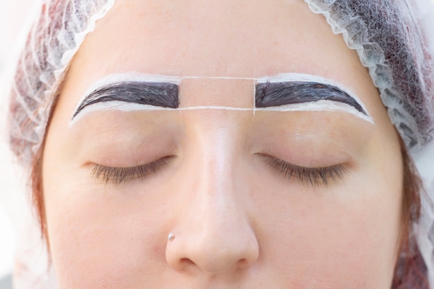 Foto teñido de cejas. salón de belleza. la niña yace con los ojos cerrados en el procedimiento de teñido de cejas. el maestro de cejas aplica el pincel a las cejas del cliente.