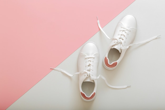 Tênis branco com atacadores voadores, sapatos femininos de couro branco com atacadores no fundo rosa. par de tênis elegantes. calçados femininos, modernos, esportivos e confortáveis. vista superior com espaço de cópia.