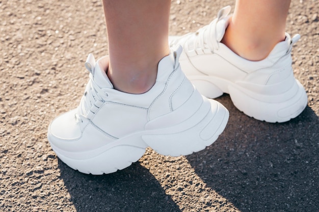 Tênis branco nas pernas da menina no asfalto
