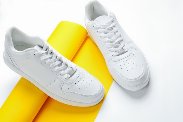 Tênis branco sobre rolo enrolado de papel amarelo. Moda minimalista