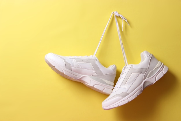 Tênis da moda modernos pendurados em cadarços em um fundo colorido