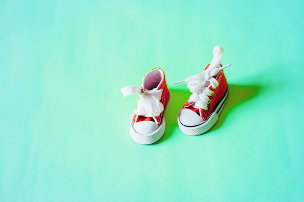 Tênis de bebê vermelho minúsculo fofo com atacadores brancos, isolados em um fundo de cor menta, com espaço de cópia para o texto, tiro aéreo. Sapatos em miniatura.