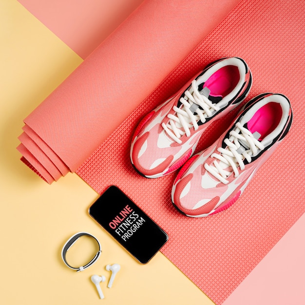 Tênis de moda brilhante com smartphone, pulseira de fitness e tapete de ioga rosa. App para treinos internos. Programa de condicionamento físico online. Treino online em casa.