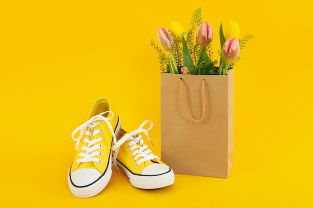 Tênis e saco de papel com flores em fundo amarelo