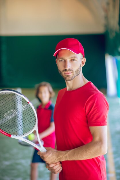 Tenista. Joven barbudo con una gorra roja de pie con una raqueta de tenis