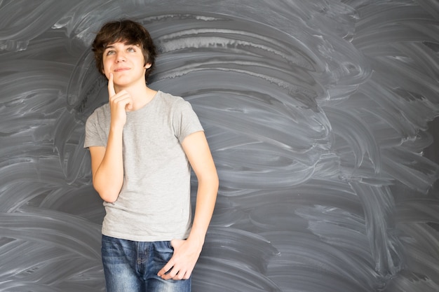 Foto tennage boy denkt und bekommt eine idee mit leerer tafel im hintergrund