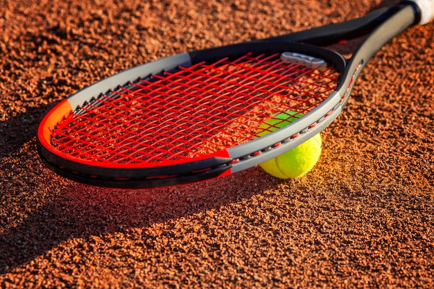 Tennisschläger mit einem Ball in der Nähe des Netzes auf dem irdenen Platz. Sonniger Tag. Nahansicht.