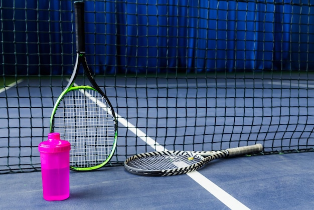 Tennisschläger und eine Wasserflasche gegen ein gespanntes Tennisnetz in einer Tennishalle Horizontales Foto