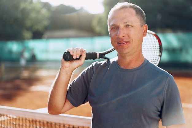 Tennisspieler mittleren Alters mit Schläger, der auf Platz nahe Netz steht